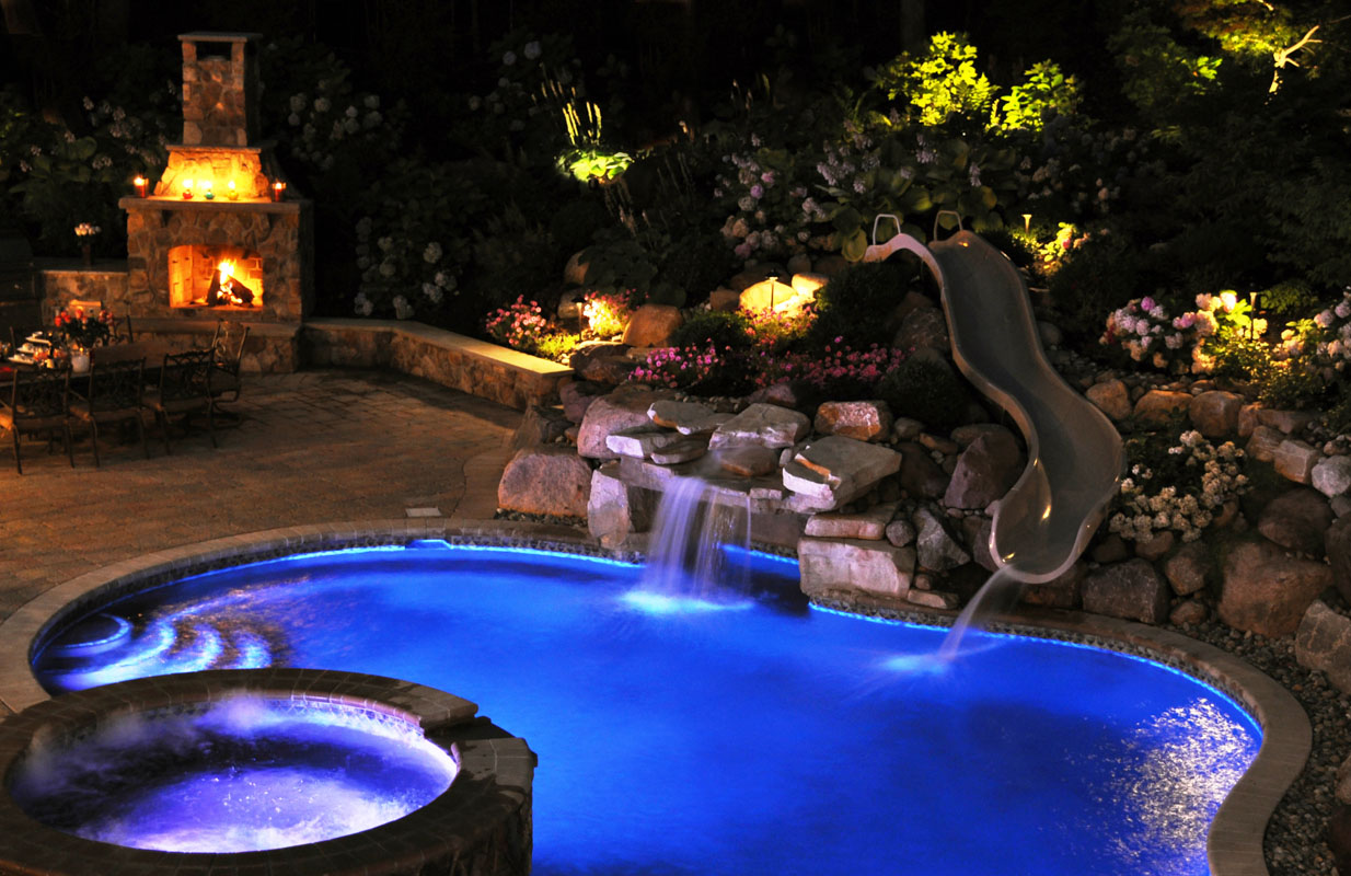swimming pool with spa and slide lit up at night