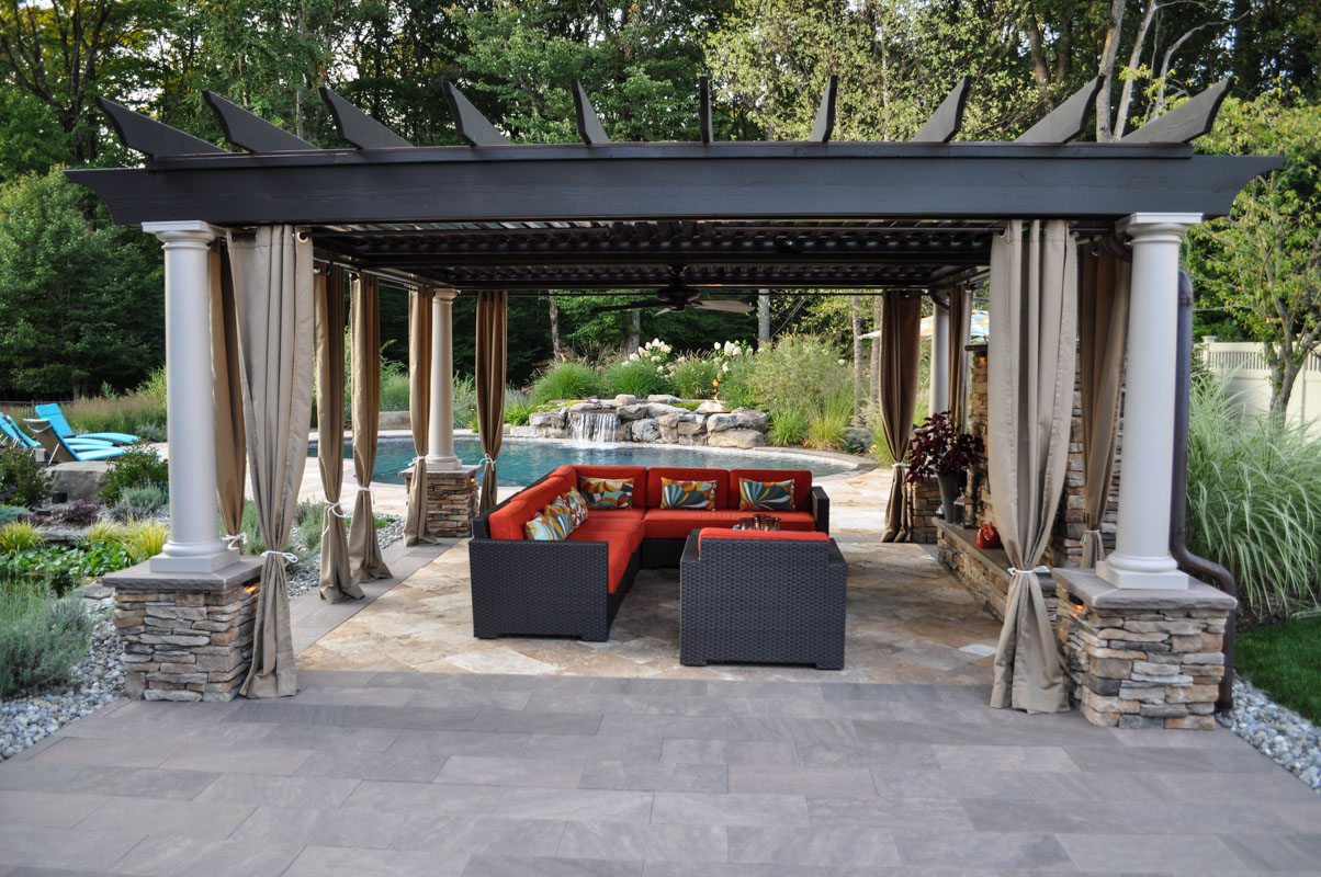 pergola with gas fireplace in foreground and custom swimming pool in background - north jersey
