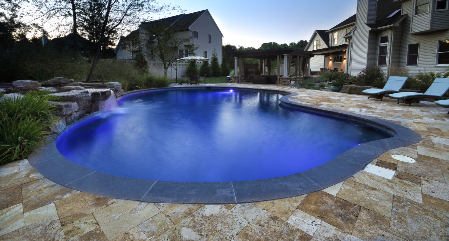 travertine and brownstone pool patio, beautiful custom swimming pool, pergola in background - north jersey