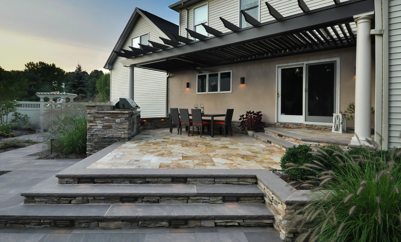 travertine and brownstone patio with built-in bbq, pergola attached to house provides shade - north jersey