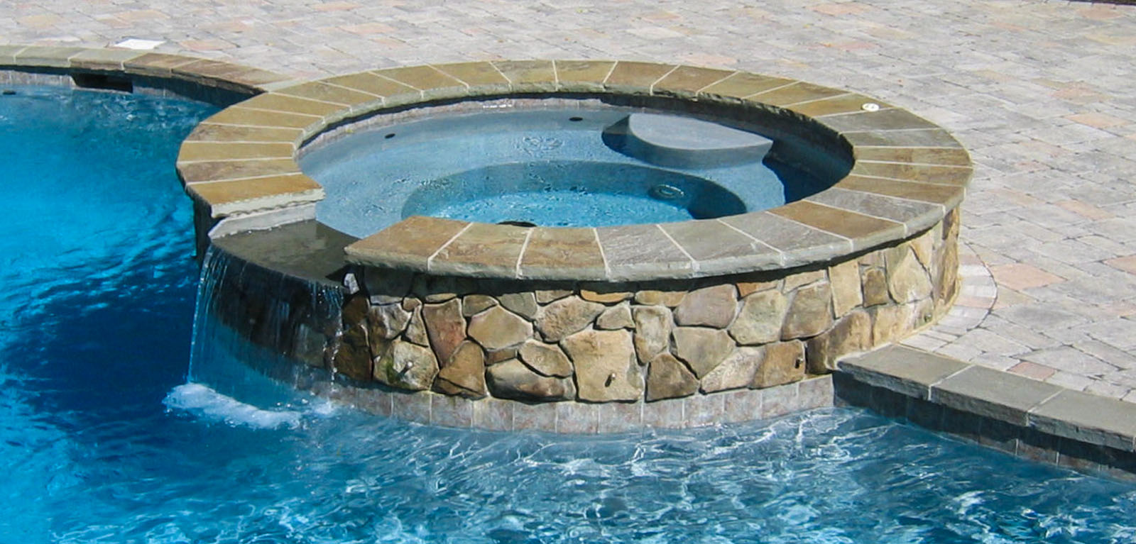 round natural stone spa with spillway into pool