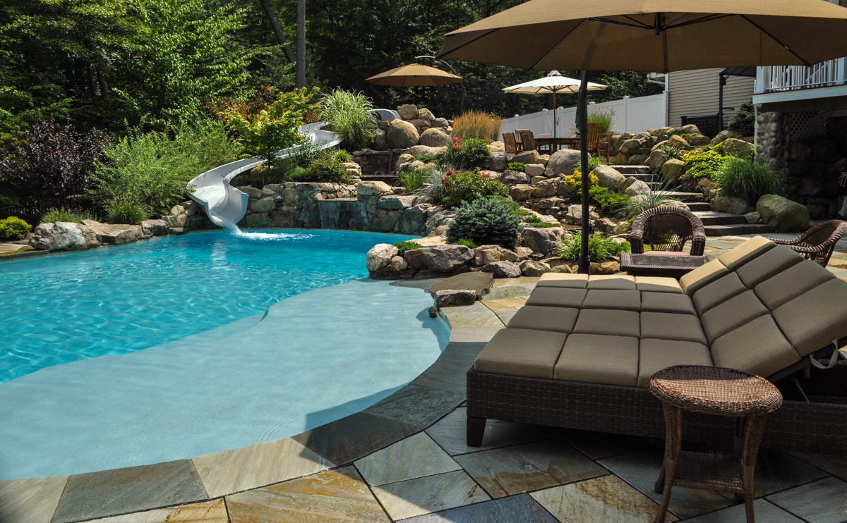 custom swimming pool with waterslide, spa, and natural stone patio