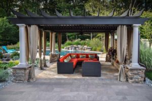pergola with gas fireplace in foreground and custom swimming pool in background - north jersey