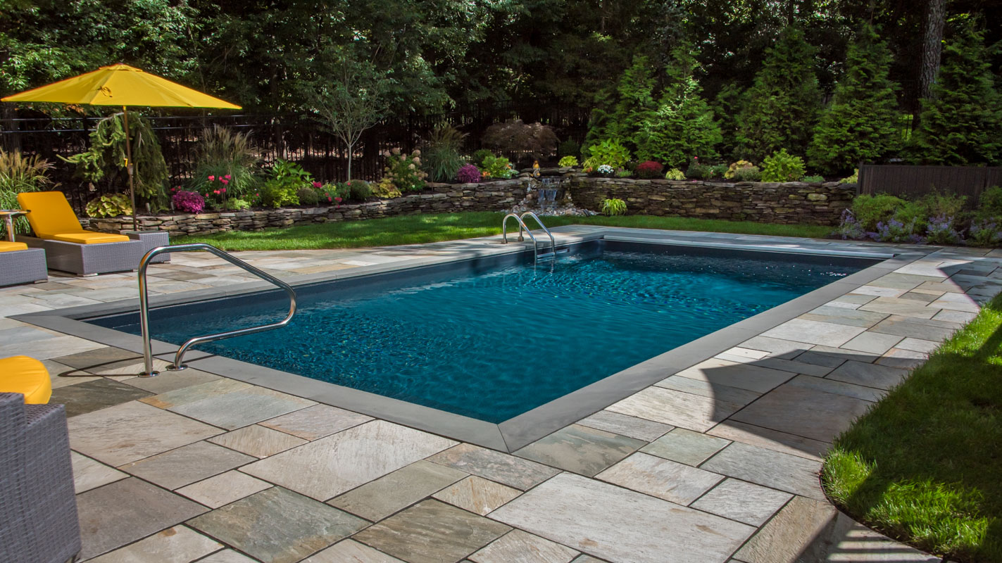 rectangular vinyl swimming pool with water feature and plantings in background