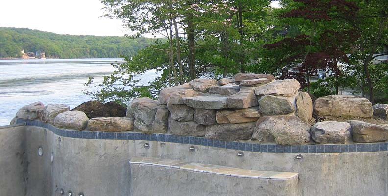 Before and after of a backyard transformed from an empty lawn into a curving poolscape with spa, stone waterfall, and natural bluestone patio.