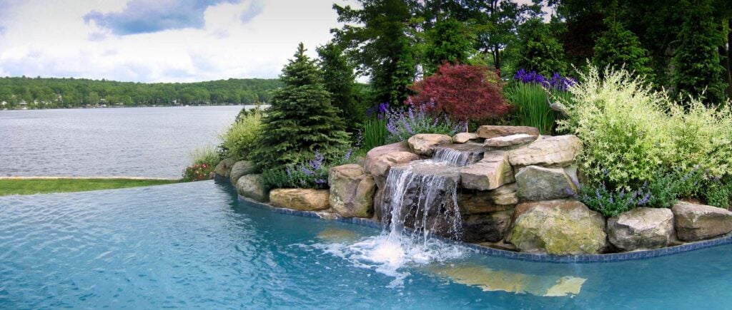 Before and after of a steep lakeside yard transformed into terraced stone steps with layered plantings, ornamental grasses, and a modern lakefront home.