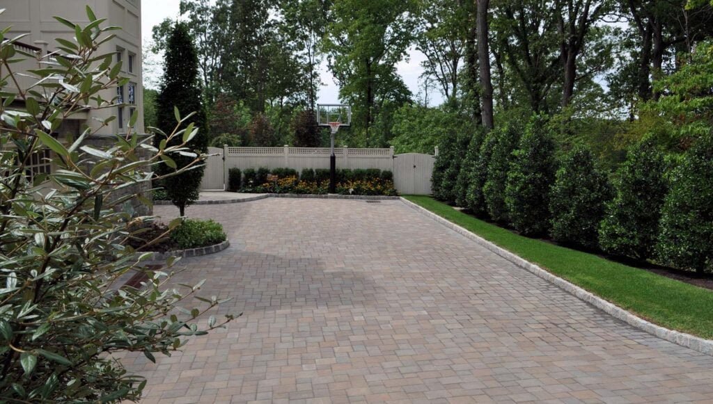 Finished backyard with custom paver basketball court, privacy fence, and manicured landscaping