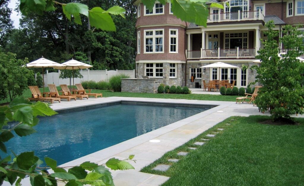 Before and after of a backyard landscape showing the transformation from a plain slope to a structured space with a curved stone retaining wall and layered plantings.