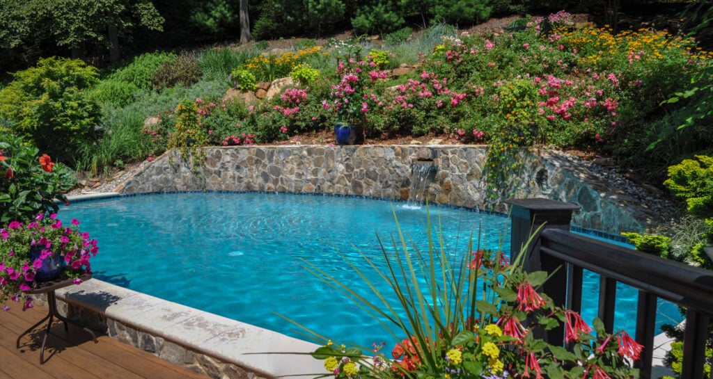 Backyard pool with stone retaining wall, waterfall feature, and vibrant flowering garden in New Jersey