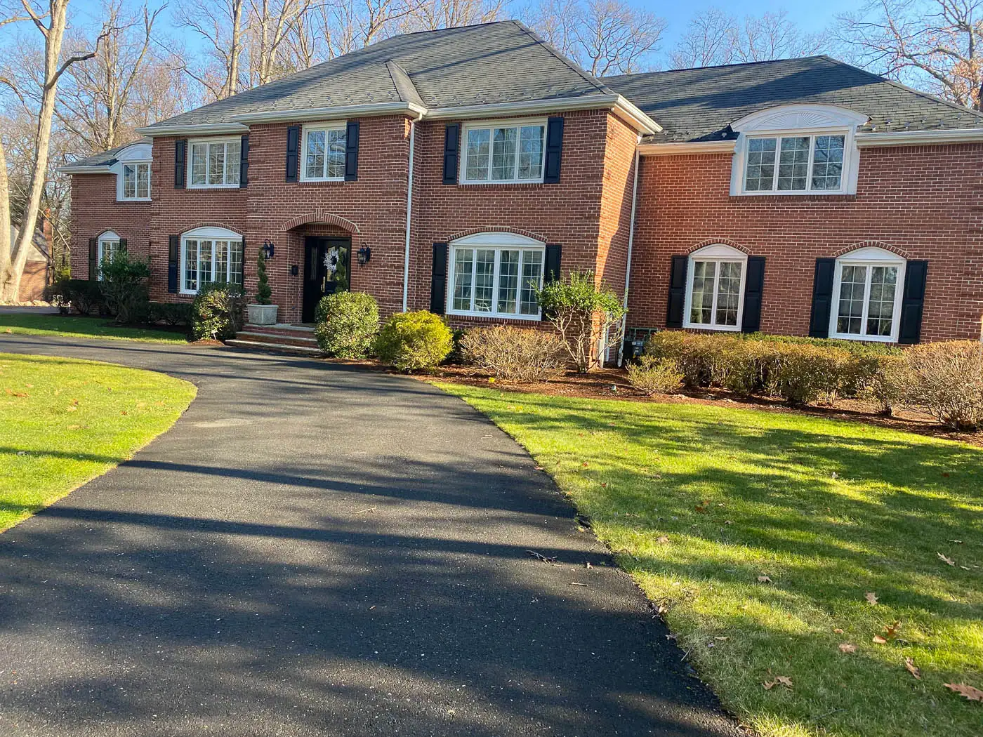 Front yard foundation planting by award‑winning CLC Landscape Design in Franklin Lakes, NJ—semicircular driveway bordered with structured boxwoods, seasonal perennials, and vibrant alliums, creating an elegant and functional garden frame.