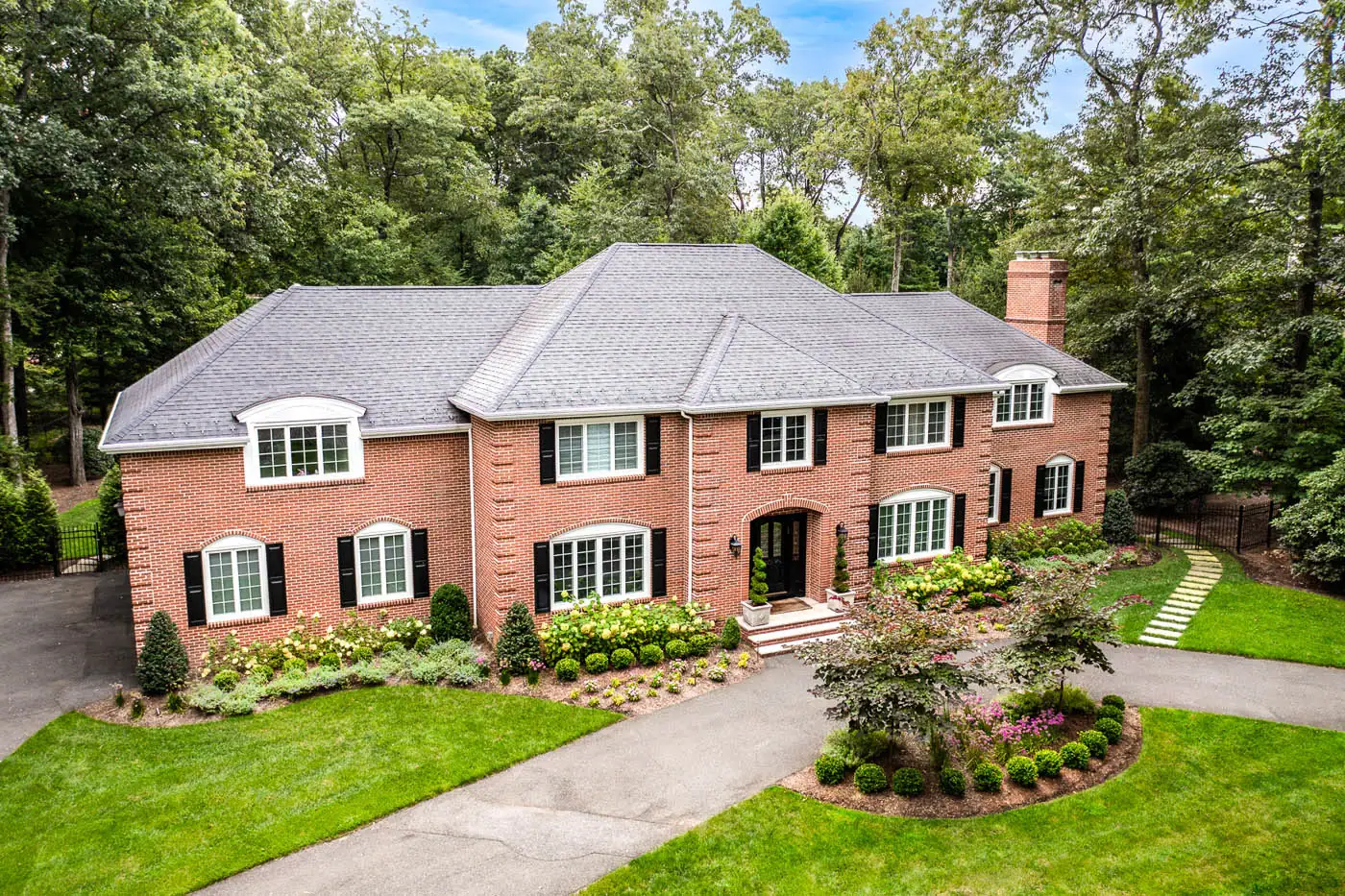 Front yard foundation planting by award‑winning CLC Landscape Design in Franklin Lakes, NJ—semicircular driveway framed by lush boxwoods, layered perennials, and seasonal alliums, creating a structured yet vibrant foundation garden