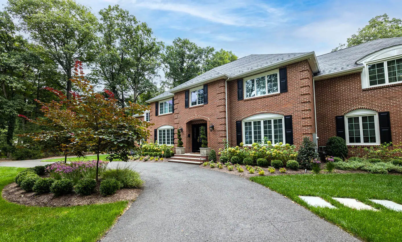 Award‑winning foundation planting by CLC Landscape Design in Franklin Lakes, NJ—vibrant alliums, structured boxwoods, and lush forest‑floor perennials layered along the front yard foundation and driveway edge for lasting curb appeal.”