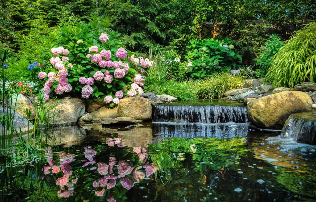 Award‑winning design‑build landscape by CLC Landscape Design in Ringwood, NJ—dual aquascape systems featuring streams, multi‑tiered waterfalls, and reflective ponds edged with lush perennials, creating a serene waterscape focal point