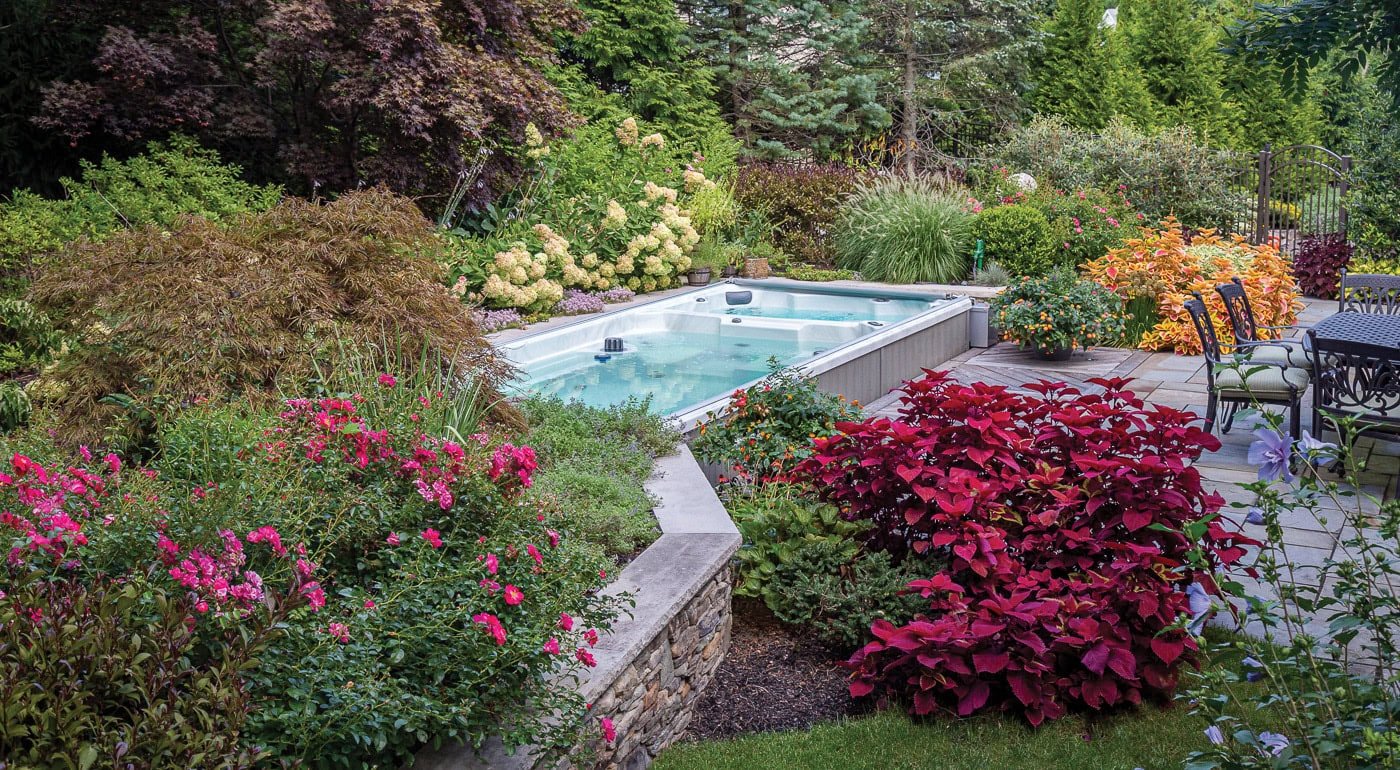 Custom hot tub and swim spa integrated with natural stone elements and bold plantings in a Franklin Lakes, NJ landscape by CLC.