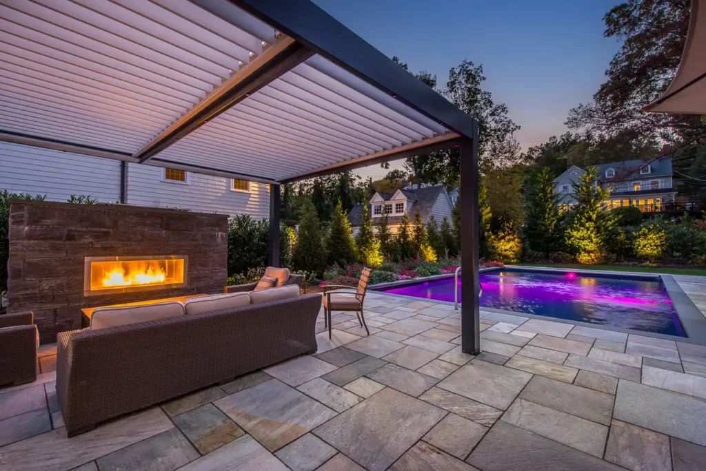 Custom backyard with swimming pool and fire pit in Montclair, New Jersey by CLC Landscape Design featuring luxury hardscaping, ambient lighting, and a complete outdoor living experience