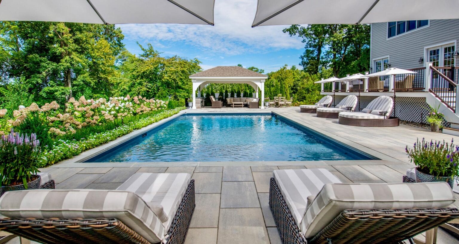 Custom backyard swimming pool design in New Jersey by CLC Landscape Design featuring modern paver patio, landscaped greenery, and a luxury pool with ambient lighting at sunset